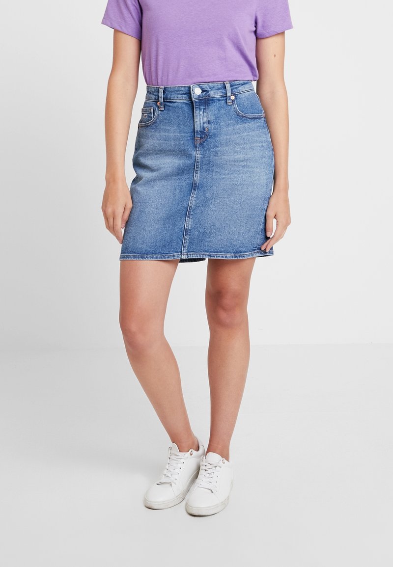 Gonna di jeans azzurro chiaro con taglio dritto, vita alta e cucitura frontale. Abbinata a una t-shirt viola e sneaker bianche.