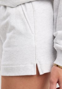 Vaaleanharmaat puuvillasekoitehousut, joissa on väljät leikkaukset. Niissä on sivutaskut, hienovarainen tekstuuri ja sivuhalkiot helmassa.