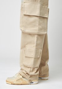 Beige cargobroek met meerdere zakken en een relaxte pasvorm, gecombineerd met crèmekleurige sneakers met een gestructureerde bovenkant en zichtbare demping.