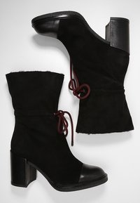 Black suede ankle boots with a rounded toe, raised heel, and elastic drawstring detail. Leather accents on toe and heel.