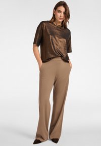 Bronze kortærmet top med skinnende tekstur, kombineret med beige, vidde bukser. Outfitet har en afslappet pasform og subtil halsudskæringsdesign.