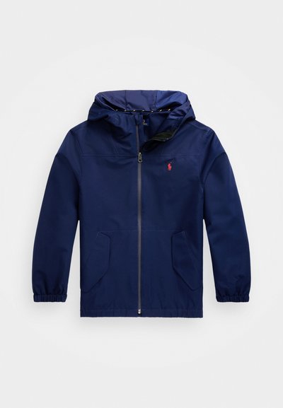 Dunkelblauer Windbreaker mit Kapuze, elastischen Bündchen, Reißverschluss vorne, zwei vorderen Taschen und einem roten Logo auf der linken Brust.