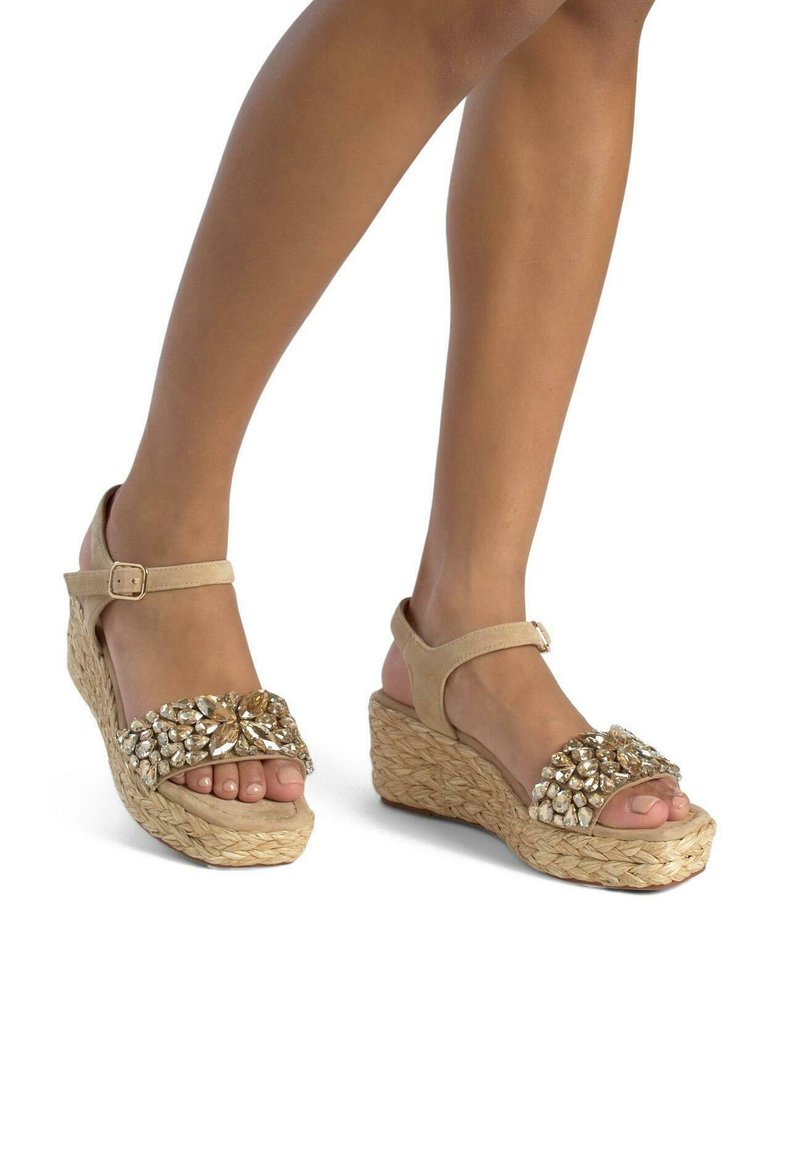 Beige Keilsandalen mit einer Espadrille-Stil Jutebasis. Das Obermaterial verfügt über einen dekorativen, mit Juwelen besetzten Riemen. Verstellbarer Knöchelriemen für den optimalen Sitz.