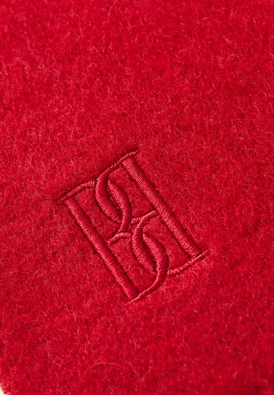 Tissu en feutre rouge avec un logo brodé en rouge assorti, présentant une texture lisse et des coutures régulières.