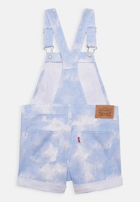 Blå denimoverall med ett molnigt mönster, justerbara axelremmar, guldfärgad hårdvara och en brun läderetikett på bakre midjan.