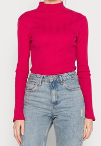 Tajta långärmad polotröja i ljusrosa ribbad tyg. Kombineras med högmidjade ljusblå jeans som har lätt slitage.