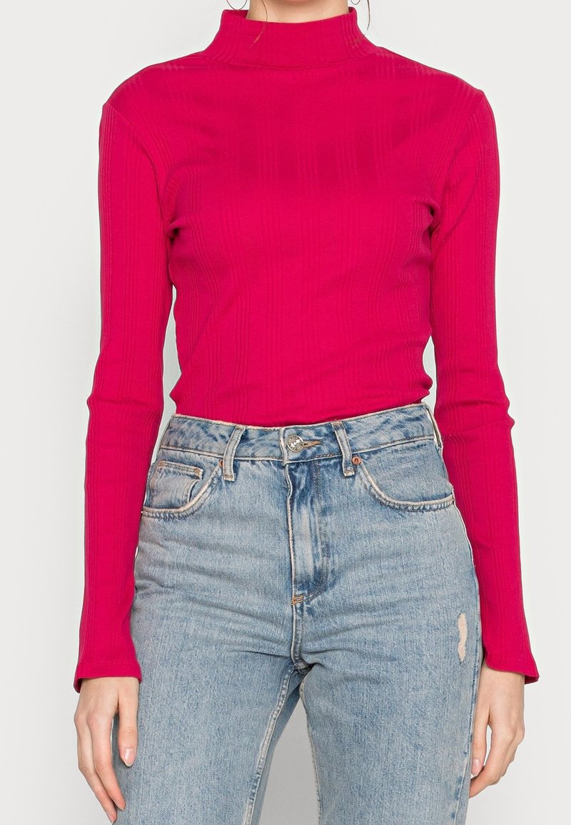 Tajta långärmad polotröja i ljusrosa ribbad tyg. Kombineras med högmidjade ljusblå jeans som har lätt slitage.