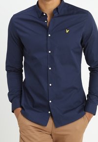 Marineblauwe longsleeve shirt van katoen. Heeft een button-down kraag, witte knopen en een klein geel arendlogo op de borst.