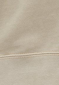 Gros plan sur un tissu beige montrant un tricot texturé et une couture horizontale avec détail de piqûre.