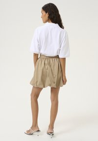 Tricou alb supradimensionat asociat cu o fustă bej pliată, cu o textură fină. Sandale cu toc cu bretele negre și albe completează look-ul.