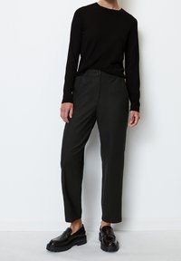 Zwarte lange mouwen shirt, aansluitende silhouet. Donkergrijze broek met een losse pasvorm en knopen aan de voorkant. Glanzende zwarte loafers met een grove zool.