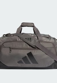 Borsa da viaggio grigia realizzata in materiale resistente, con un logo nero e tracolla regolabile. Include una tasca frontale con zip e dettagli testurizzati.