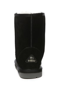 Black suede ankle boot with a soft white lining, flat rubber sole, and a triangular logo patch at the heel. Features stitched seams.