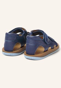 Sandali in pelle blu navy con lati aperti, cinturini regolabili e suole in gomma marrone. Finitura testurizzata con branding prominente sulla suola.
