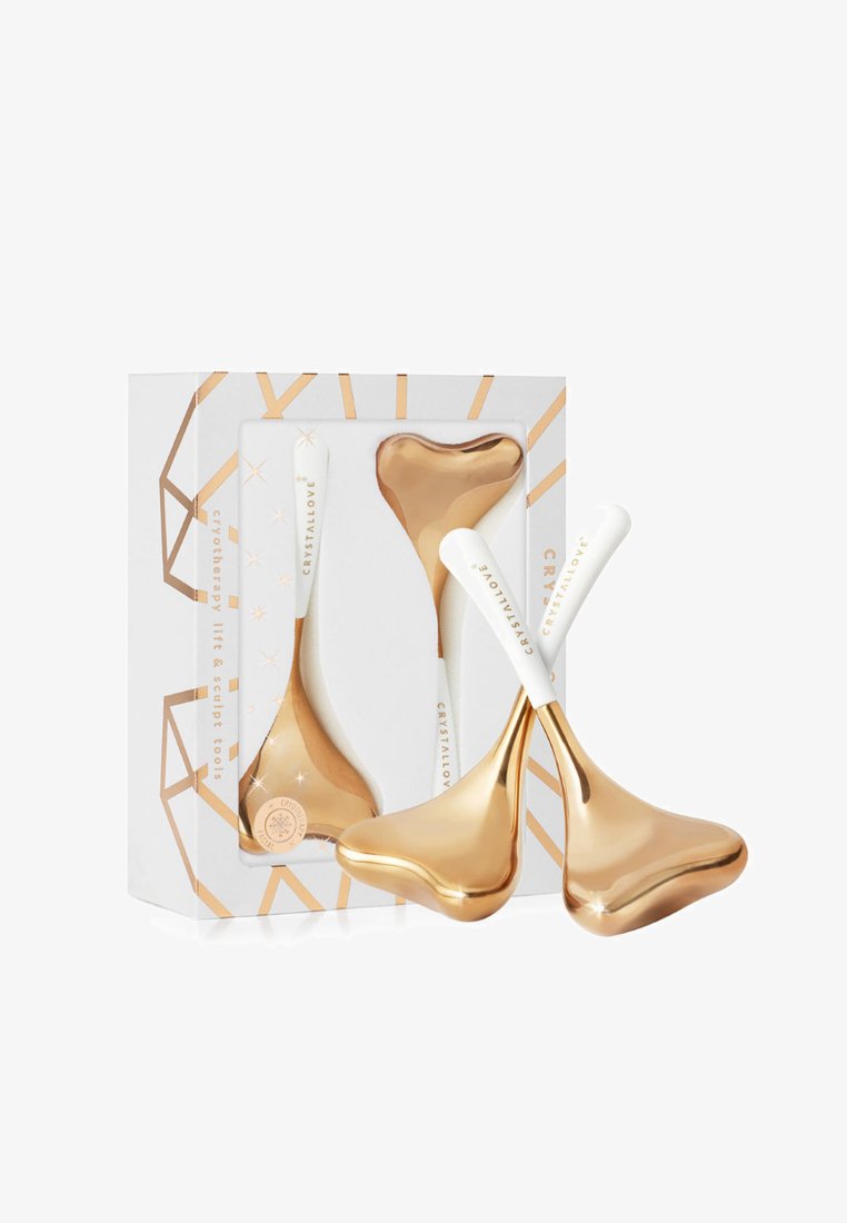 Złote wałki do twarzy w kształcie serca i owalu. Białe ergonomiczne uchwyty z napisem "CRYSTALLOVE". Zapakowane w pudełko o geometrycznym wzorze.