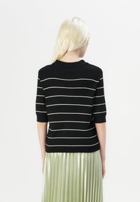 Maglione a righe nere con maniche corte, decorato con righe orizzontali color crema e colletto a coste; abbinato a una gonna plissettata verde.