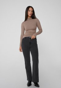 Langärmliges, eng anliegendes braunes Oberteil, kombiniert mit hoch taillierten, weit geschnittenen schwarzen Jeans. Schwarze Knöchelstiefel vervollständigen den lässigen Look. Glatte Stofftextur.
