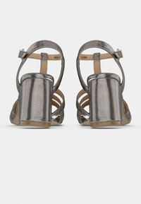 Metāliskas sudrabotas sandales ar augstiem papēžiem, biezs papēdis, atvērta purngala daļa un potītes siksniņa. Aprīkotas ar izgriezumu dizainu un gludu tekstūru.