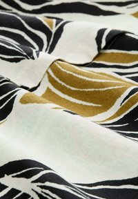 Stof met een bloemmotief, kenmerkend door gedurfde zwarte lijnen, een crème achtergrond en gouden accenten; textuur, middelzware katoenmix.