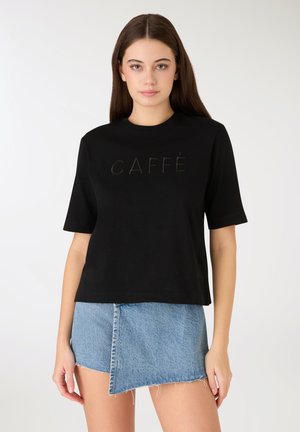 Czarna bawełniana koszulka z krótkim rękawem, z wypukłym napisem "CAFFÈ". Połączona z postrzępioną spódnicą dżinsową, oba elementy o casualowym stylu.