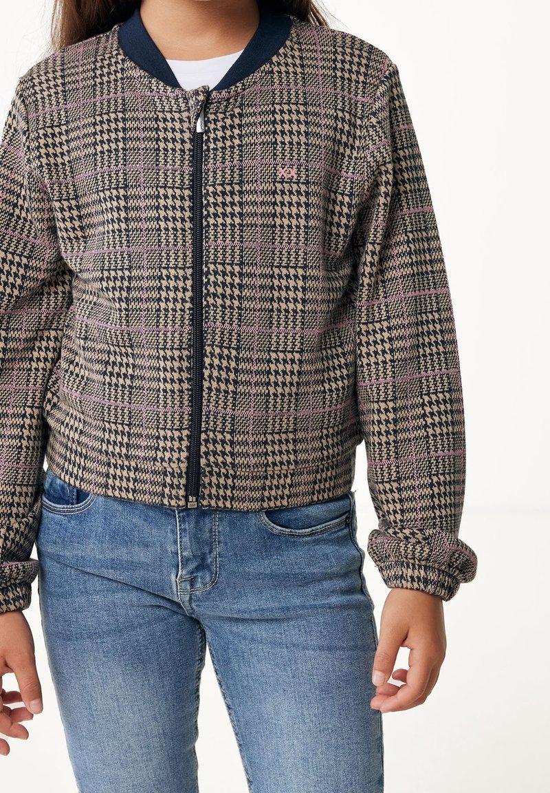 Hnědo-modrá bomber bunda s kostkovaným vzorem, se zipem vpředu, žebrovaným límcem a elastickými manžetami. Nositá přes bílou košili a modré džíny.