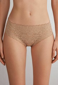 Nude kleur hipster ondergoed van kant met bloemenpatronen, voorzien van golvende randen en een comfortabele pasvorm. Zachte textuur en intrigerend ontwerp.