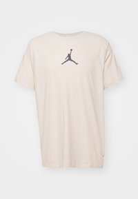 Camiseta de algodón beige de manga corta y escote redondo. Presenta un logotipo oscuro de Jordan impreso en la parte delantera. Sin patrones ni herrajes adicionales.