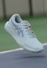 Světle modrá sportovní bota s prodyšnými akcenty, texturovaným povrchem a vzorovanou podrážkou. Obsahuje šedé logo a růžový akcent na jazyku.