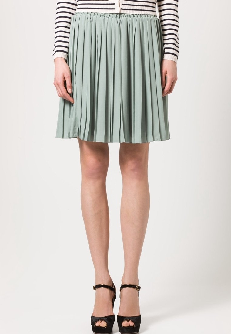 Falda plisada verde claro hecha de tela suave, con una cintura elástica, combinada con tacones plataforma negros y una blusa a rayas.