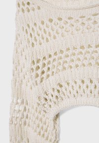 Gros plan sur un tissu ajouré crème avec des motifs alternant losanges et côtes, montrant la texture et les détails des points.