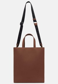 Brązowa skórzana torba typu tote o minimalistycznym designie, z dwoma górnymi uchwytami oraz czarnym, regulowanym paskiem z wypukłym napisem.