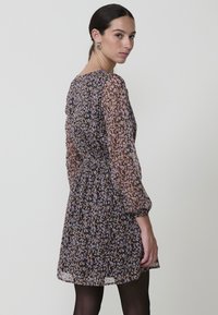 Vestido con estampado floral, de mangas largas y transparentes, con cintura fruncida y un dobladillo corto. Presenta una mezcla de colores morado, rosa y beige.