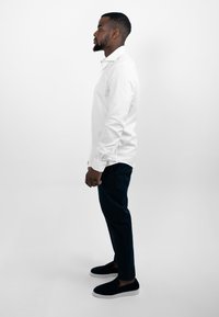 Witte overhemd met knopen, donkergekleurde broek en zwarte instappers. Het overhemd heeft een klassieke kraag; gladde stof; getailleerde silhouet.