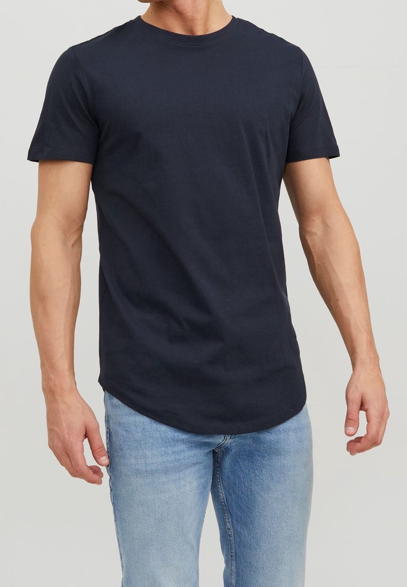 Navy blue cotton t-shirt with short sleeves, round neckline, and a slightly curved hem, worn with light blue denim jeans.