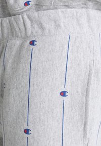 Grijze sweatpants met verticale blauwe lijnen en een herhalend blauw en rood logo patroon. Zachte textuur met een elastische tailleband.