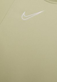Jasnozielona koszulka sportowa o gładkiej fakturze. Posiada haftowane logo Nike w kształcie łuku w kolorze białym na piersi. Prosty design, okrągły dekolt.