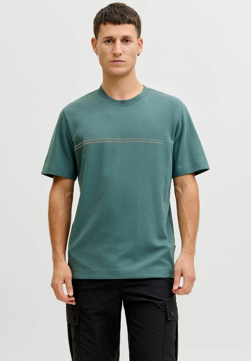 T-shirt en coton vert avec un col rond, des manches courtes et une bande horizontale sur la poitrine. Design minimaliste, coupe décontractée.