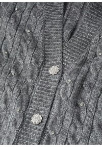 Grauer gestrickter Cardigan mit Zopfmuster, strukturiertem Stoff und runden metallischen Verzierungen auf der Vorderseite. Gerippter Kragen und Bündchen.