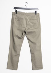 Pantaloni khaki appesi a un gancio di metallo nero. Le caratteristiche includono una vestibilità dritta, tasche posteriori e una texture liscia simile al cotone.