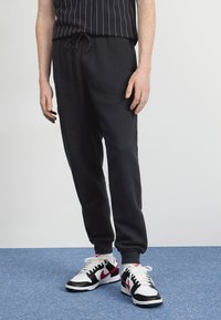 Černé tepláky s elastickým pasem a šňůrkou, se červenými bočními pruhy. Vzaty s černobílými teniskami, které mají robustní design.