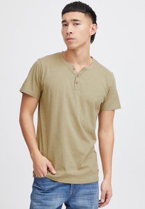 Olivgrünes kurzärmliges Henley-T-Shirt mit einem Knopfleistenverschluss und einem schlichten Schnitt. Weicher Stoff, kombiniert mit blauen Jeans.