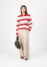 Striped long-sleeve polo in cream with red horizontal stripes. Loose beige trousers and an olive green bag. Leopard print shoes.
