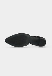 Semelle de chaussure noire à bout pointu avec grip texturé et petit talon bloc sur un fond clair uni.