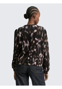 Zwarte en paarse geblokte sweatshirt met lange mouwen, verzamelde schouders en een ronde hals. Gecombineerd met donkere denim jeans.