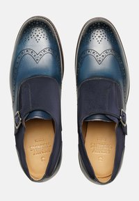 Leder Schuhe mit einem Verlauf in Blau, dekorativen Perforationen und einem Schnallenverschluss an einem marineblauen Stoffriemen.