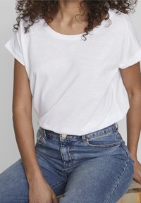T-shirt en coton blanc avec des manches courtes retroussées et une coupe décontractée, associé à un jean en denim bleu taille haute avec un bouton de fermeture.
