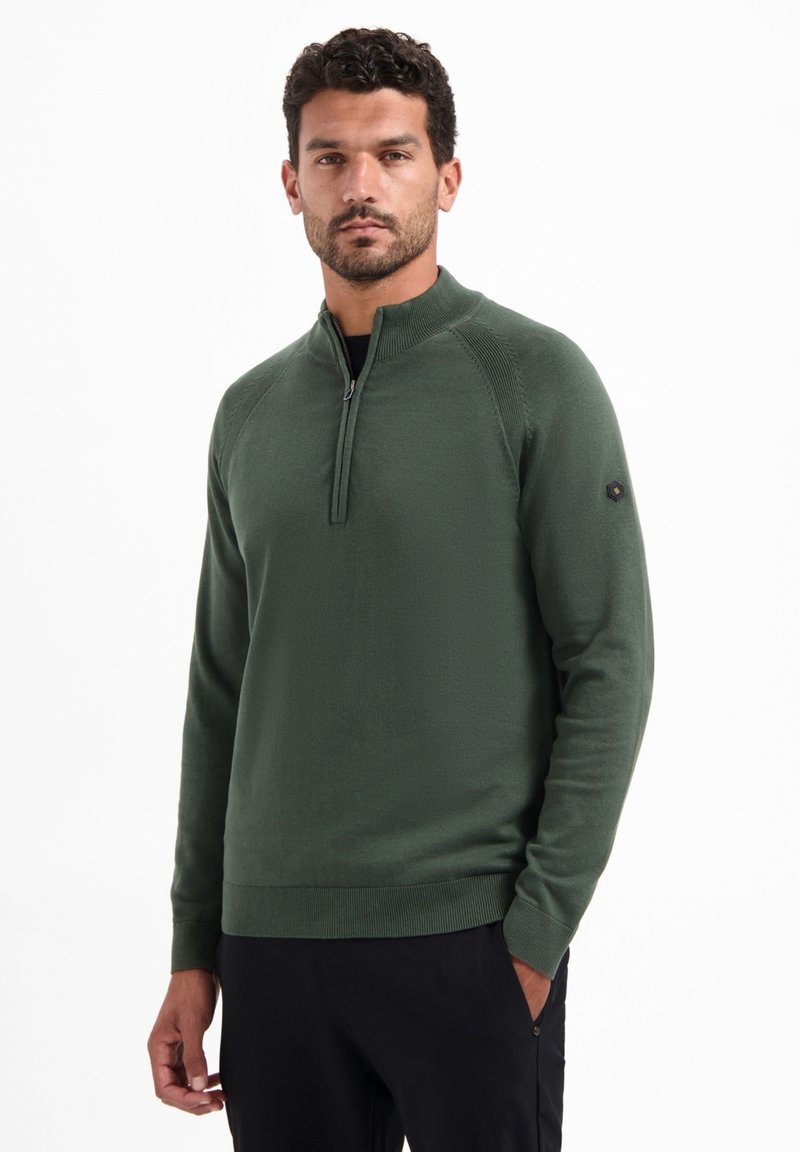 Groene pullovertrui met een hoge kraag, halve ritssluiting, geribde manchetten en onderrand, en een klein logo detail op de linkermouw.