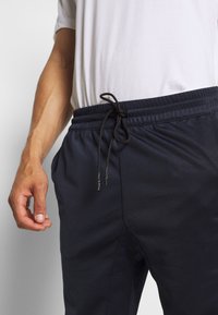 Marinblå träningsbyxor med elastisk midja och svart snörning. Har sidofickor och en slät, lätt tygtextur.