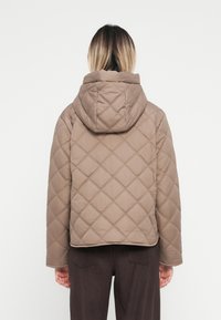 Brun vadderad jacka med huva, med en diamantmönster, kort design och mjuk textur. Bakvy visar enkelhet och rena linjer.