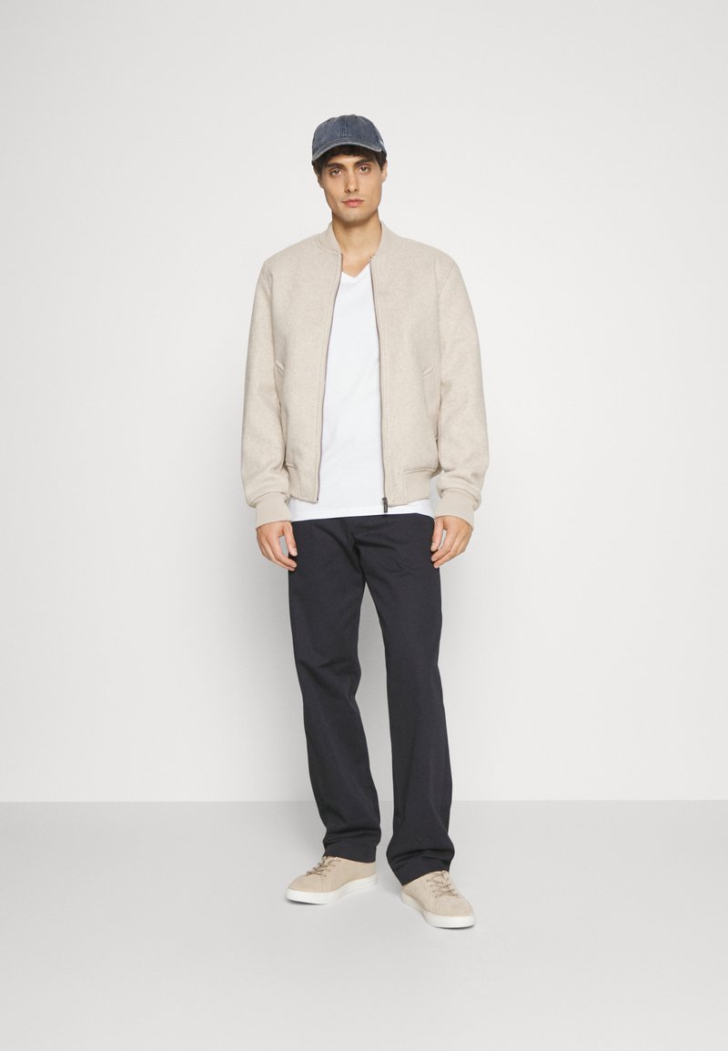 Beige bomber jacket, white t-shirt, navy trousers, and beige sneakers. Gray denim cap. Simple, relaxed fit, with a smooth texture.